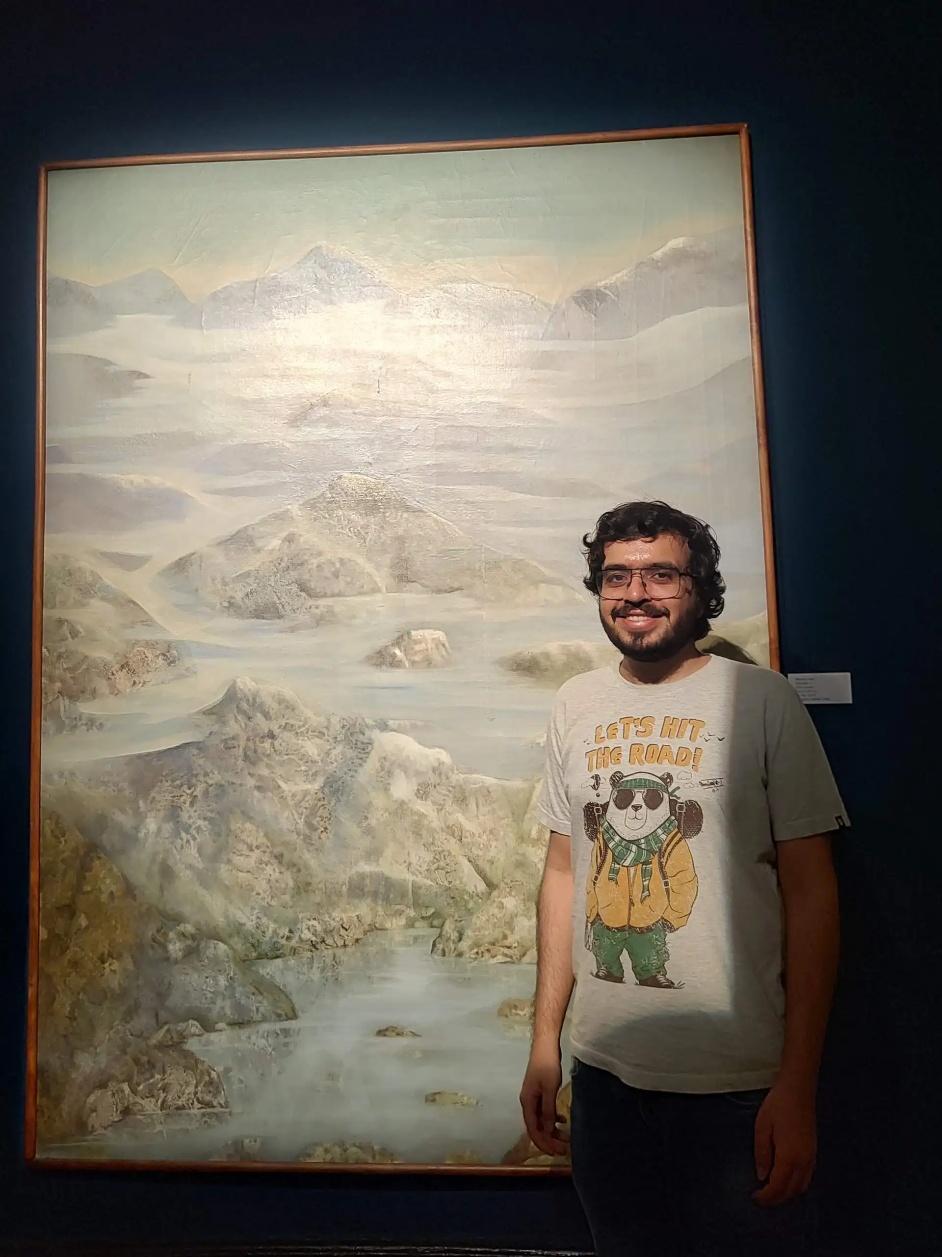 Me standing in front of a painting of mountains and a river