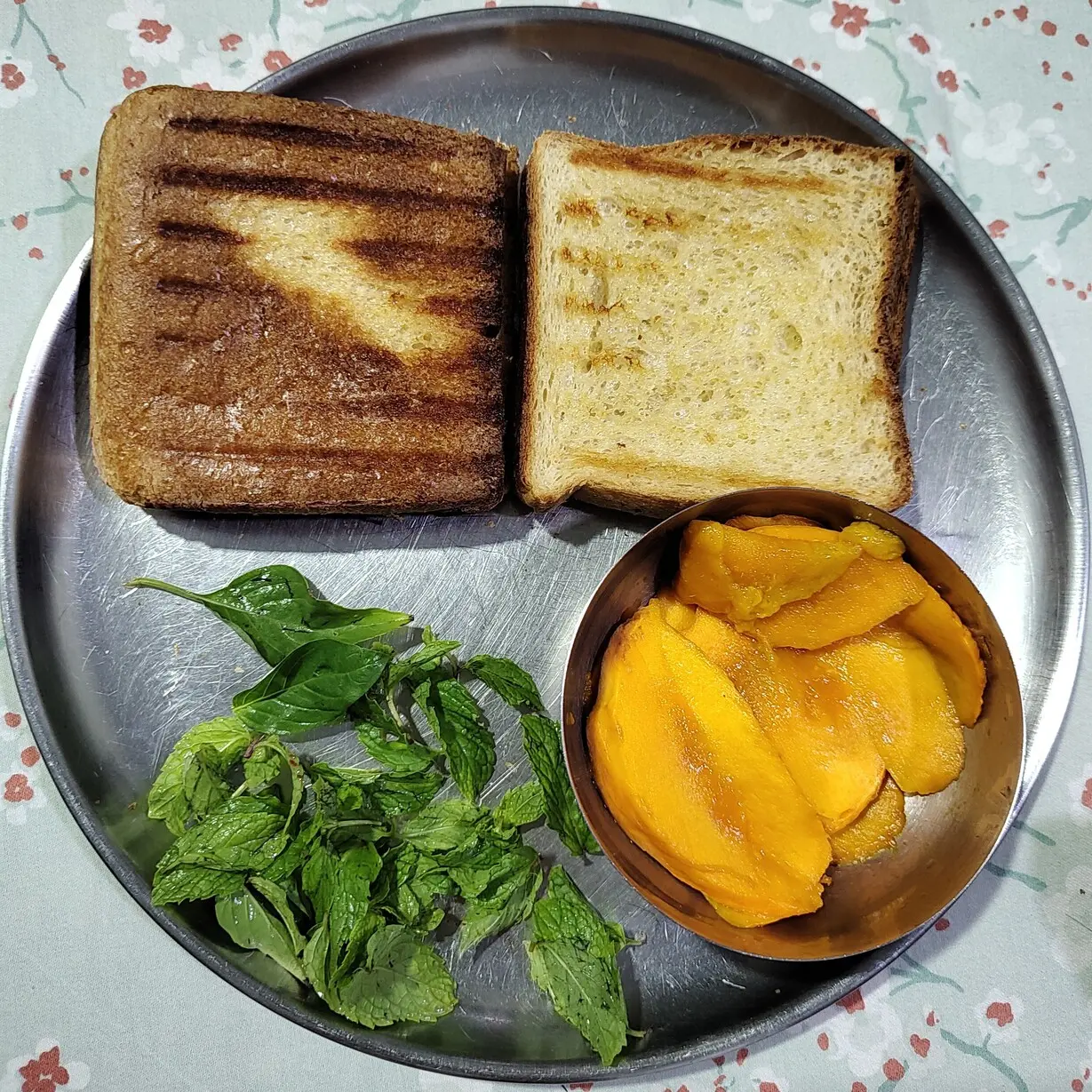 Toasted bread, mint and basil leaves, and sliced mango laid out in a plate.