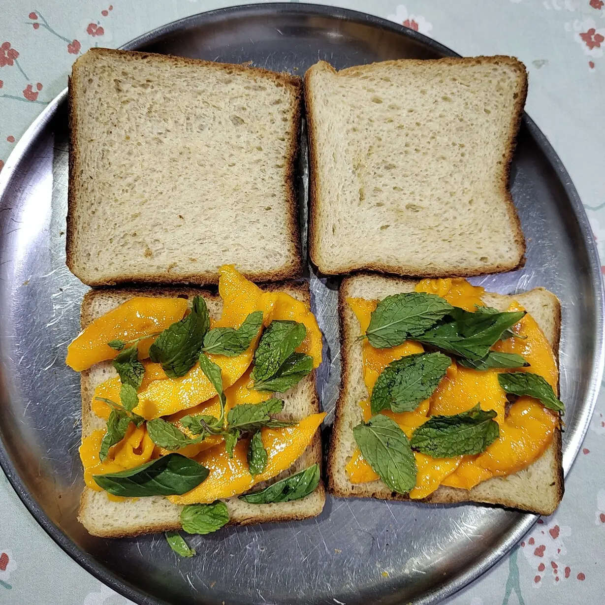 Mango slices and mint and basil leaves arranged on the bread.