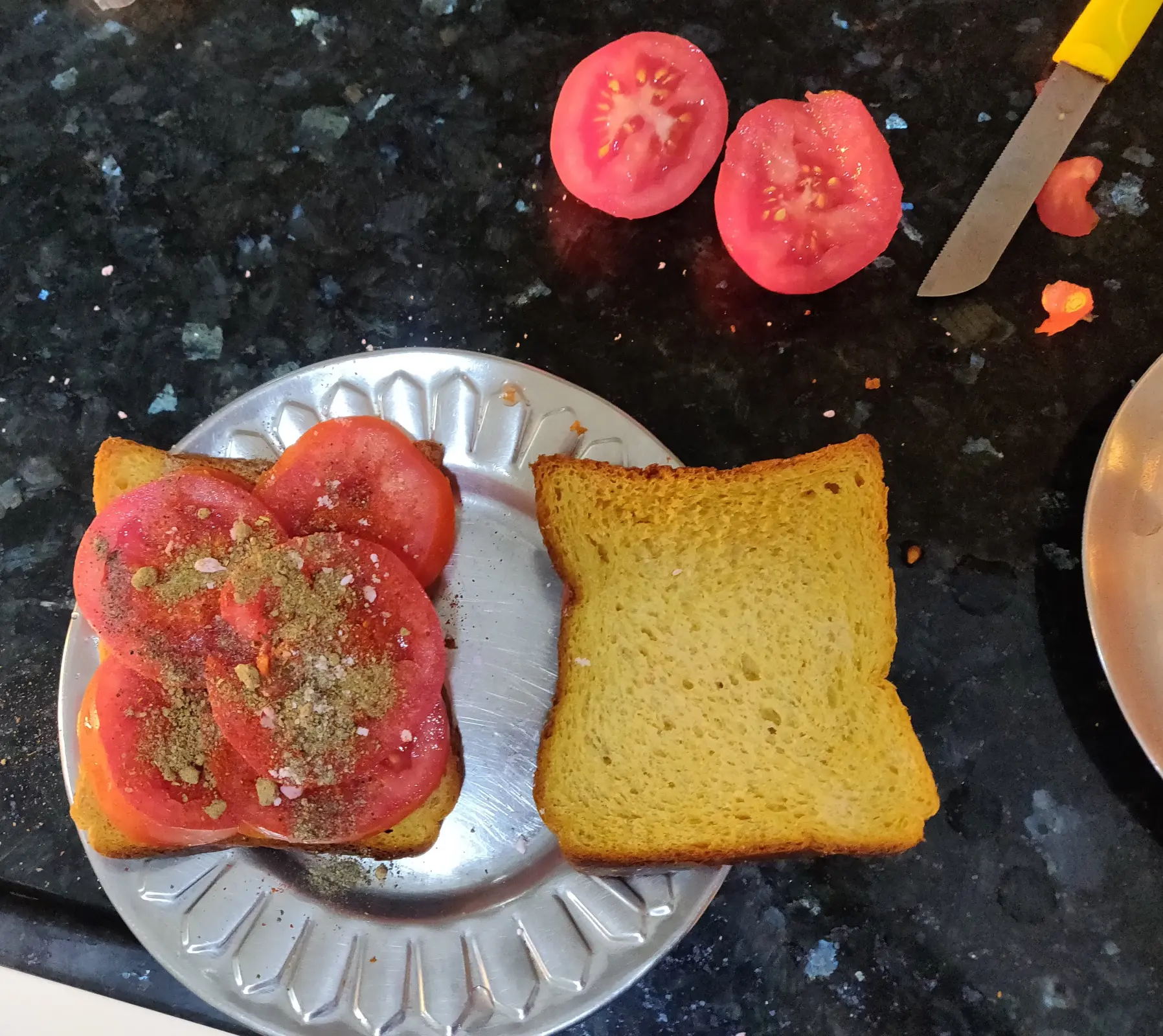 Spices sprinkled on tomato slices placed on a slice of bread.