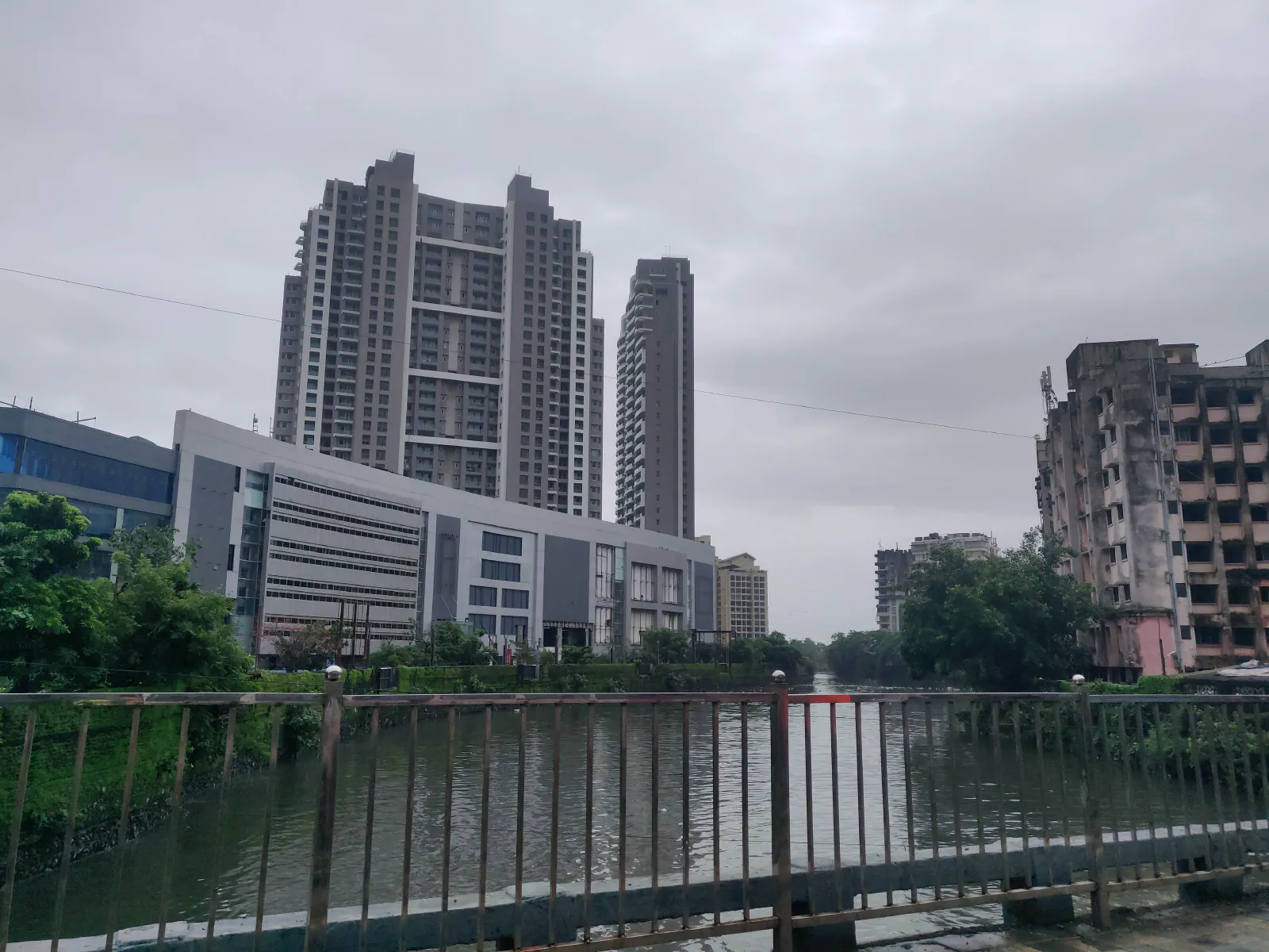 A river seen from atop a bridge. A mall and a skyscraper behind it.