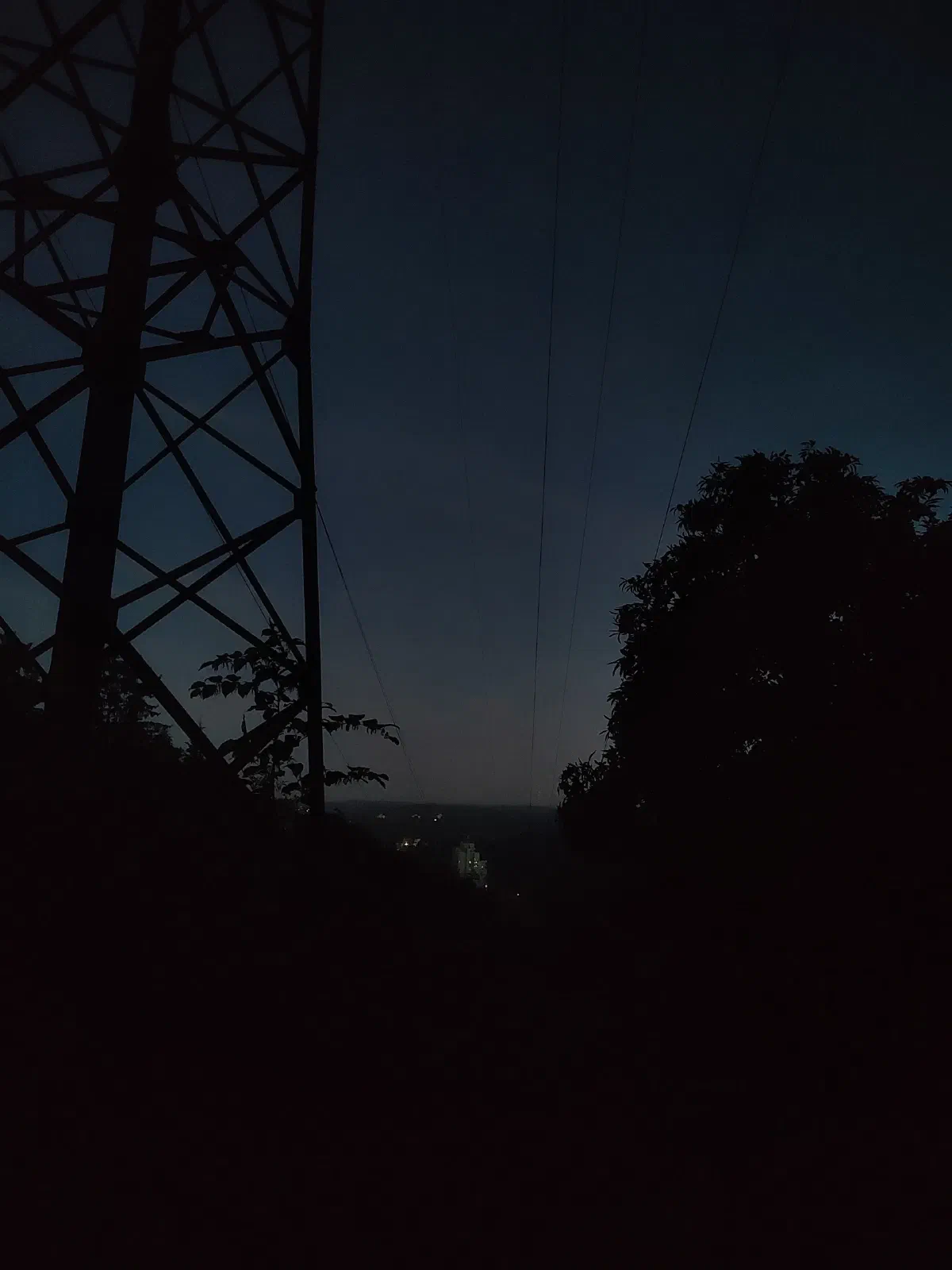 A faint silhouette of an electricity pylon and overhead powerlines against a backdrop of a dark blue sky.