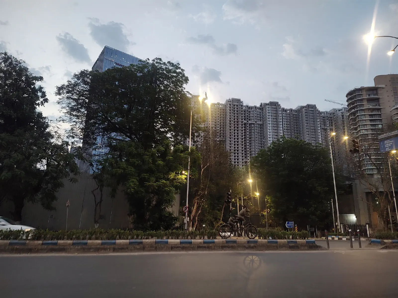 Two bunnies ride a tandem cycle on the divider. They cast a shadow on the road. 
